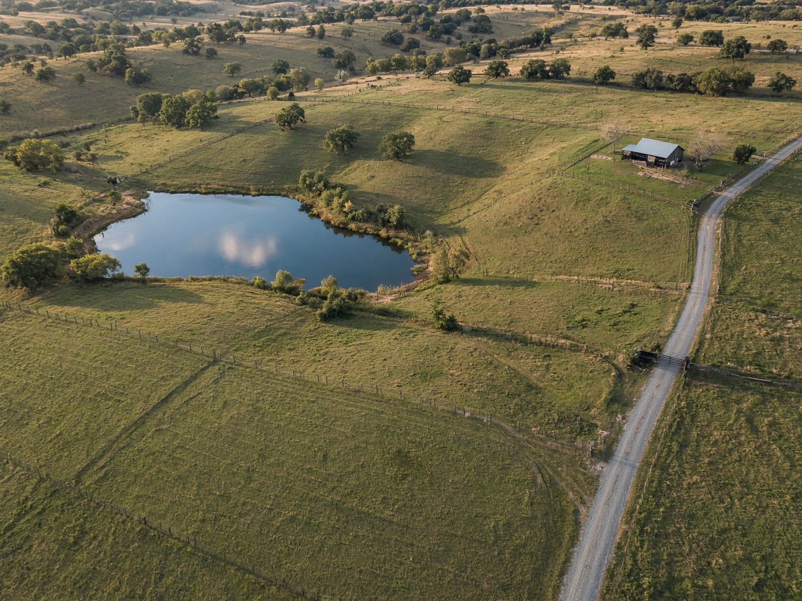 Aerial land listing photo of a North Texas ranch tract with fence lines, a pond, and a gravel road